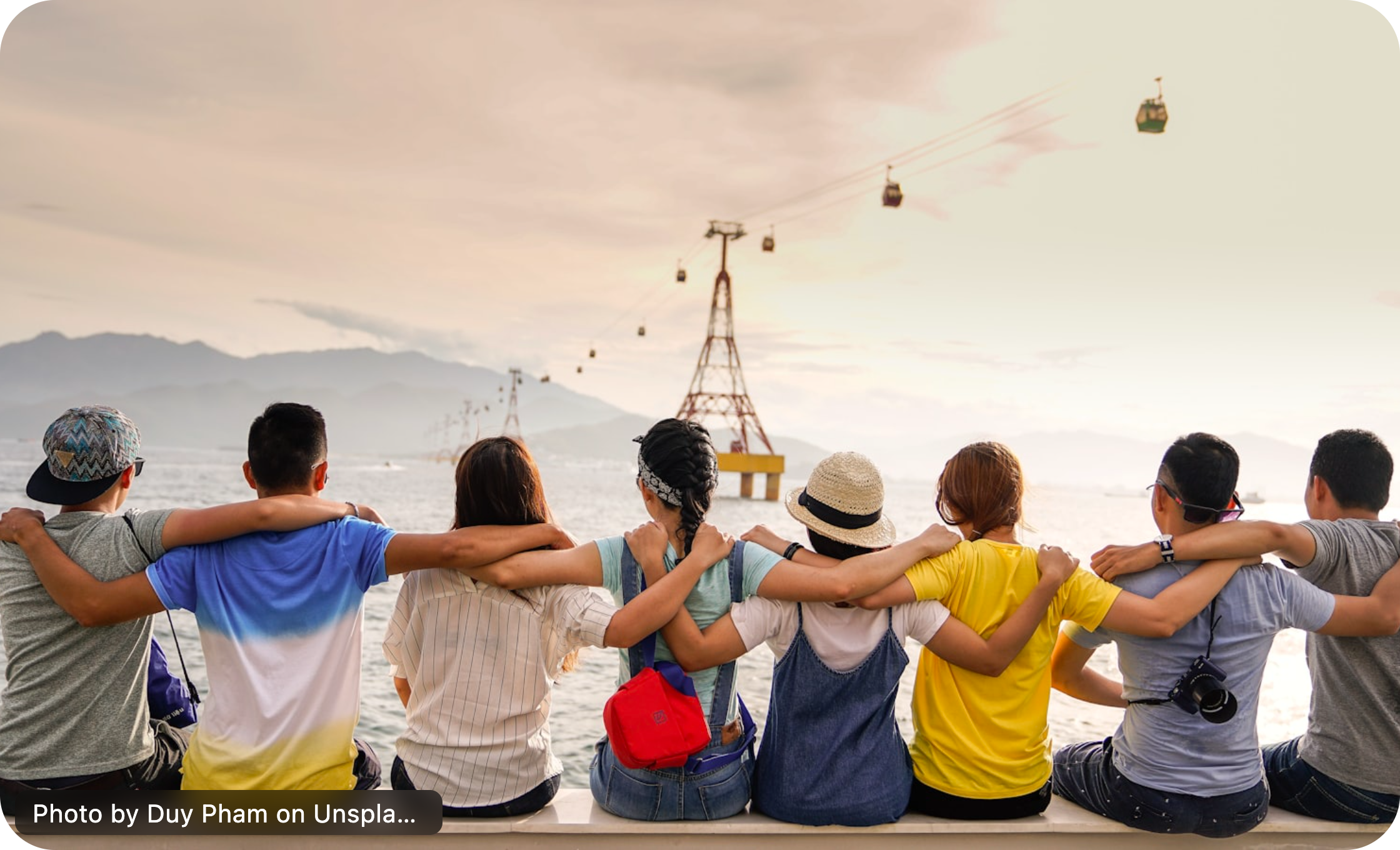 Friends sitting together with their arms around one another by the water